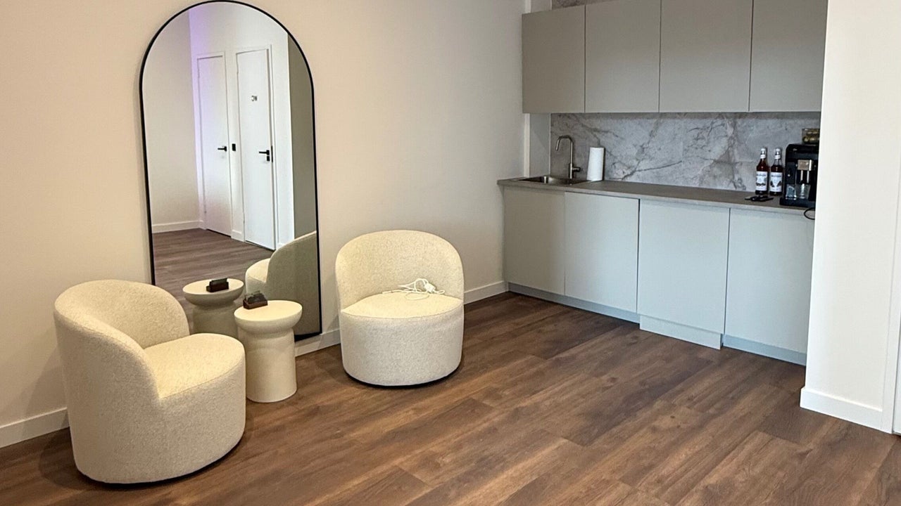 De zithoek van de salon: twee witte boucléstoelen, een bijzettafel en een staande boogspiegel